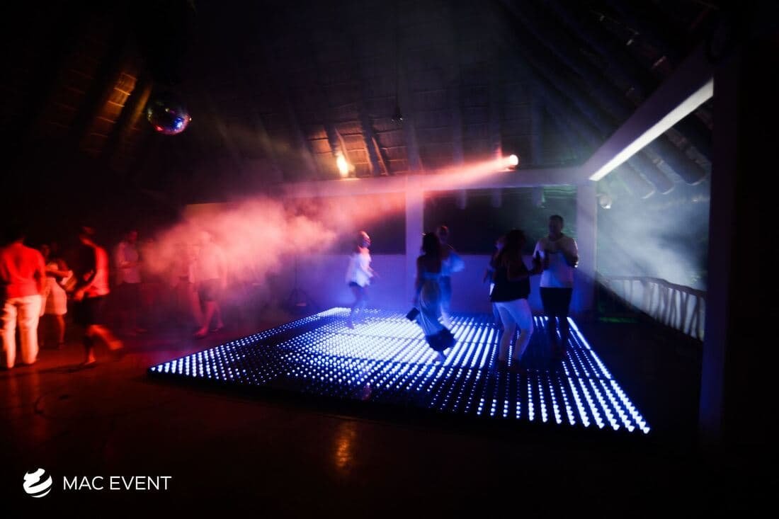 A dark, intimate dance venue with a glowing LED floor, haze effects, and soft beams of red and blue lighting, creating a visually striking atmosphere for dancing.