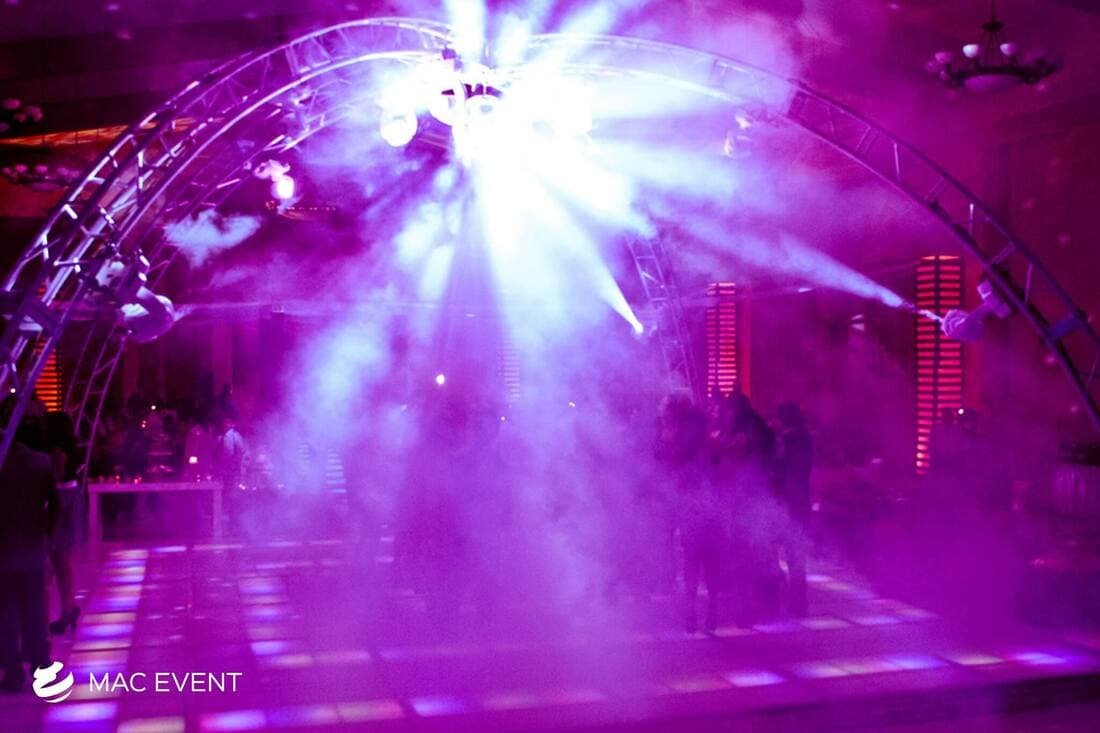 A dance floor bathed in purple light with fog effects and dazzling beams of light, setting a futuristic and energetic ambiance for partygoers.